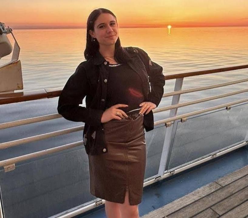 Smiling girl with hands on hips in front of sunset over a body of water